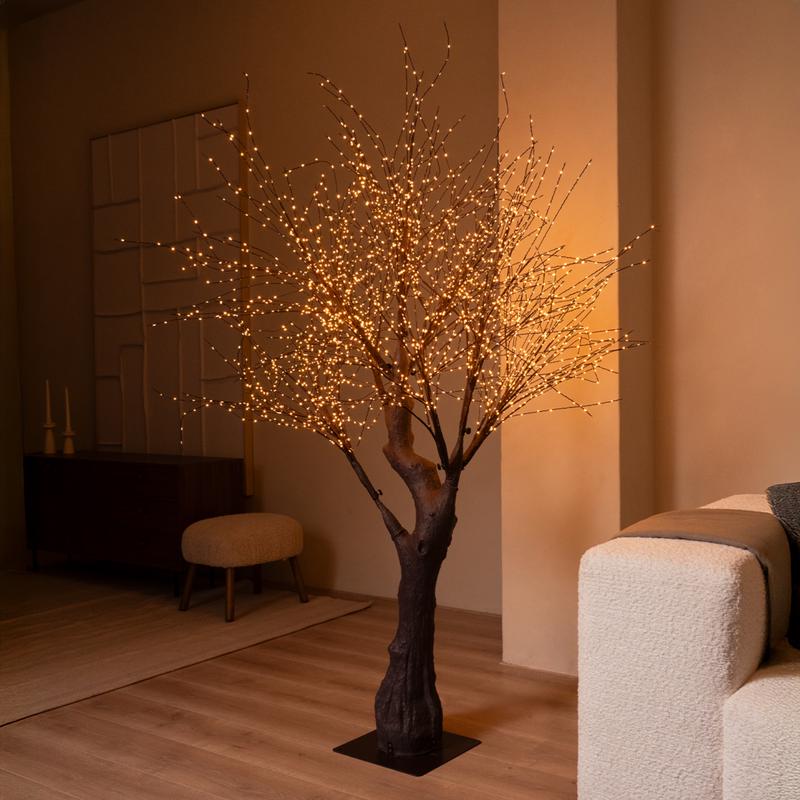 Brandende Action lichtboom met goudkleurige ledlampjes in een woonkamer naast een witte bank Brandende Action lichtboom met goudkleurige ledlampjes in een woonkamer naast een witte bank