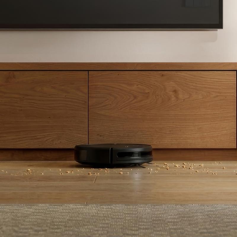 Action robotstofzuiger rijdt onder een houten tv-meubel en zuigt kruimels op Action robotstofzuiger rijdt onder een houten tv-meubel en zuigt kruimels op